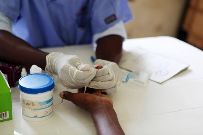 A gloved health worker taking a finger-prick blood sample at a community outreach clinic