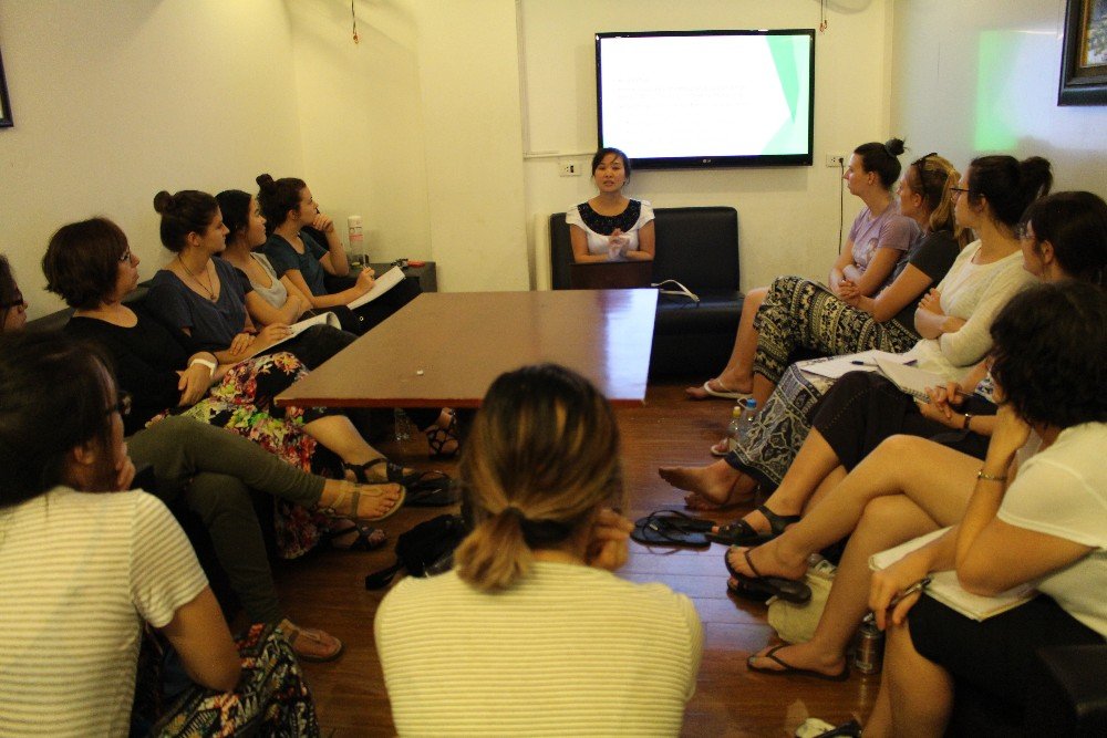 An in-country coordinator delivering a briefing to a seated student group taking notes