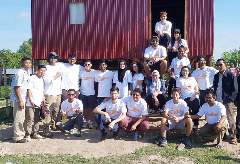 A student group standing with members of the in-country team in front of a completed raised house