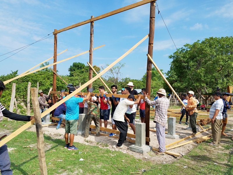Students working alongside local builders to raise the timber frame of a community building